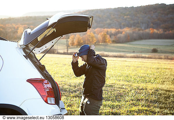 Seitenansicht eines Mannes  der einen Scheinwerfer trägt  während er im Auto auf dem Feld steht