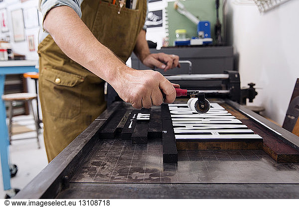 Seitenansicht eines Mannes  der in einer Druckerpresse hölzerne Alphabete malt