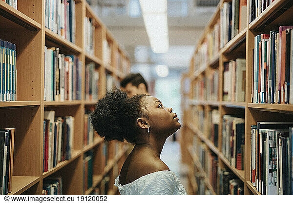 Seitenansicht eines Studenten  der in der Bibliothek der Universität Bücher im Regal sucht