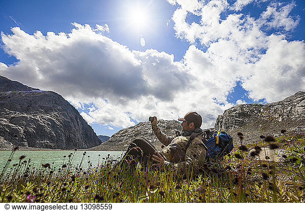 Seitenansicht eines Wanderers der beim Entspannen am Seeufer gegen den Himmel fotografiert