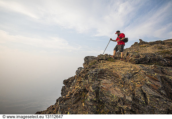Seitenansicht eines Wanderers mit Wanderstöcken am Berg vor bewölktem Himmel
