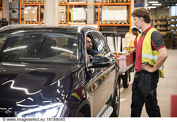 Seitenansicht von männlichem Verkaufspersonal mit Hand an der Hüfte im Gespräch mit einem Kunden im Auto an der Kasse