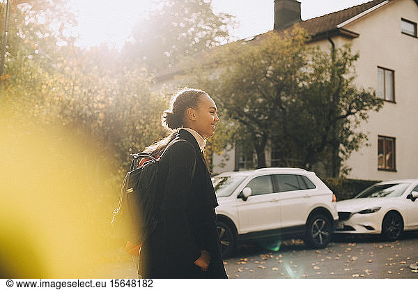 Seitenansicht von Teenager-Mädchen  die im Herbst gegen Auto und Haus laufen