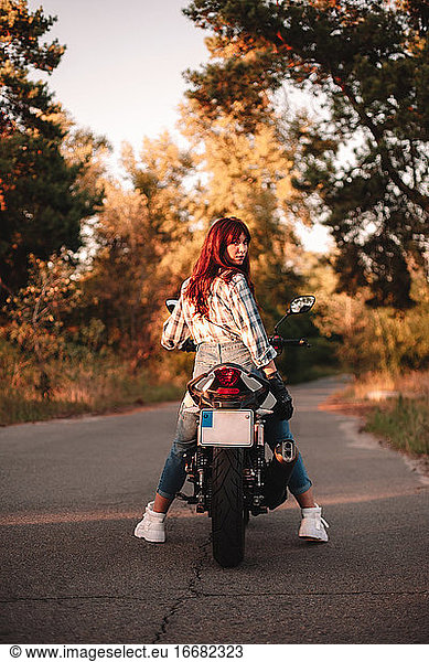 Selbstbewusste Frau  die auf einem Motorrad sitzend über die Schulter in die Kamera schaut