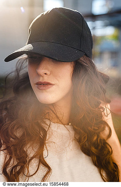 Selbstbewusste gelockte Frau  die auf der Straße eine Kappe mit Linsenreflexion trägt