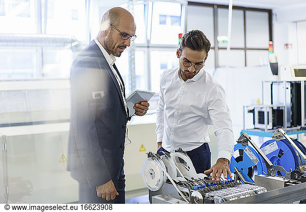 Selbstbewusste männliche Techniker  die in einer Fabrik über Maschinen gegen Maschinen diskutieren