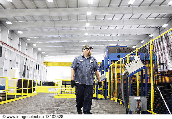 Selbstbewusster Arbeiter geht in voller Länge an Geräten in einer Fabrik der Metall-Stahlindustrie vorbei