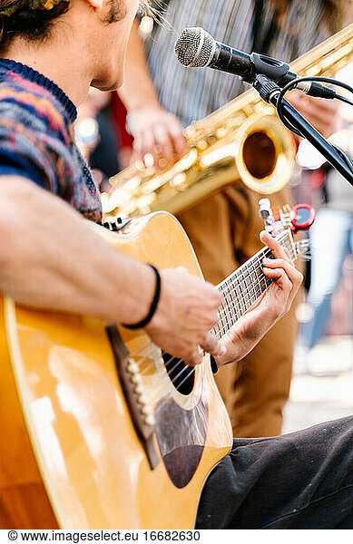 Selective focus on the hands of a young man playing a guitar in the street