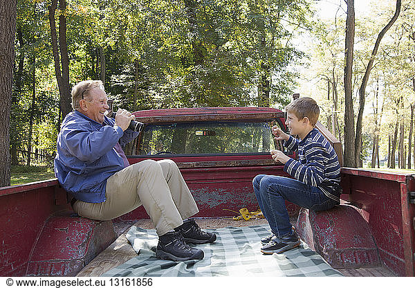 Senior and grandson sitting in back of pickup truck using binoculars