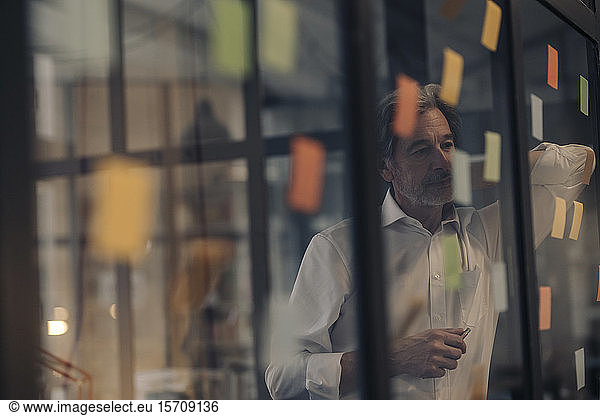Senior businessman looking at adhesive notes at glass pane in office