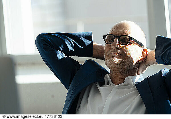Senior businessman sitting with hands behind head relaxing in office