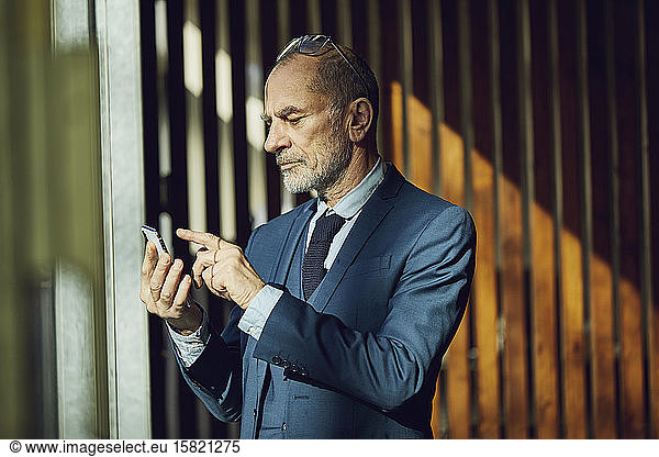 Senior businessman standing in his sustainable office  using smartphone