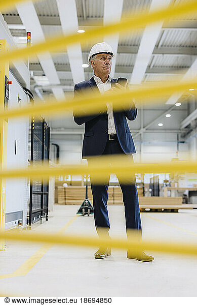 Senior businessman standing with smart phone in factory