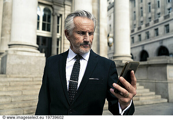Senior businessman using smart phone near building
