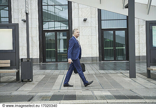 Senior businessman walking on footpath in city