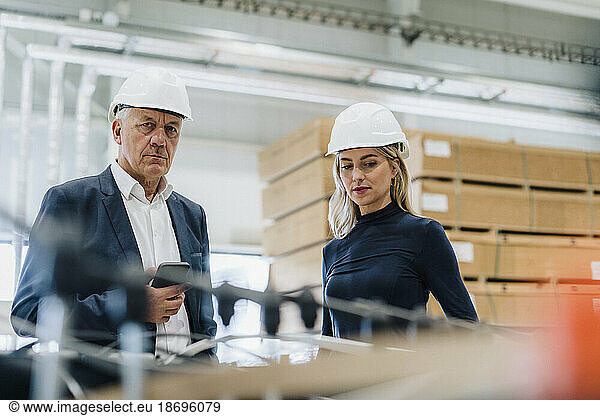 Senior businessman with colleague wearing hardhat in industry