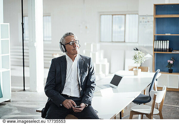 Senior businessman with eyes closed enjoying music listening through headphones in office