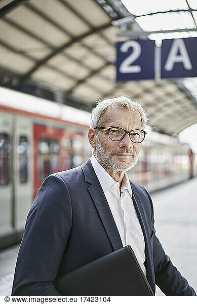 Senior businessman with laptop standing on railroad station platform