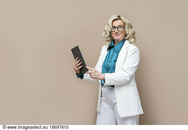 Senior businesswoman holding tablet PC against colored background