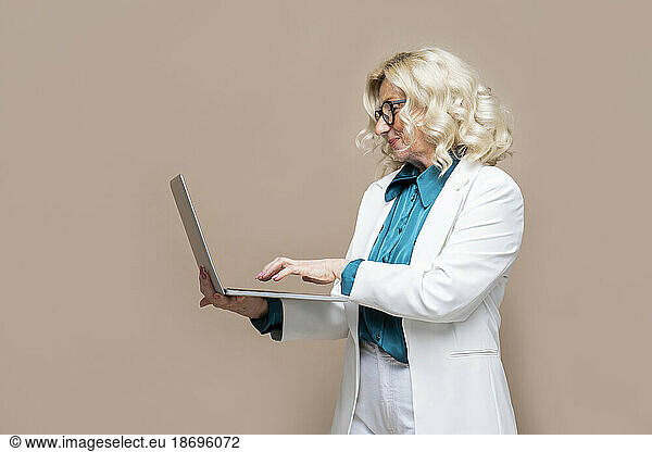 Senior businesswoman using laptop against colored background