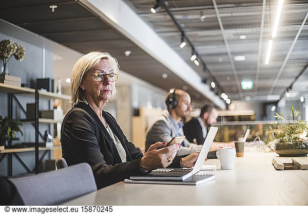 Senior businesswoman using mobile phone while working at table with colleagues in office
