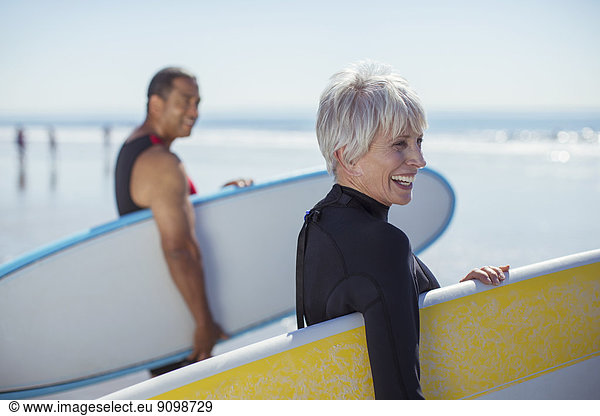 Senior couple carrying surfboards on beach