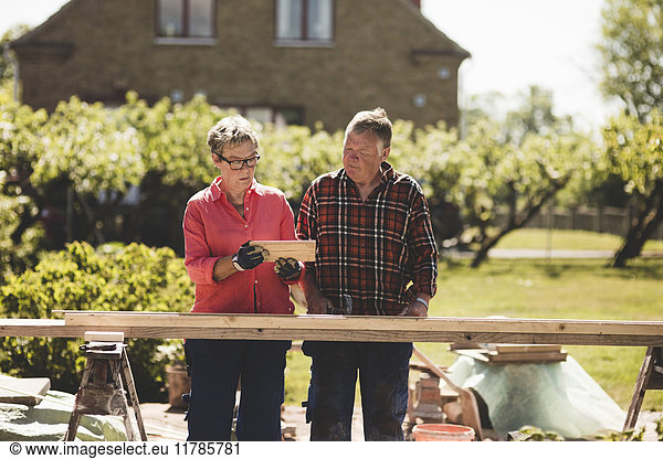 Senior couple examining wooden plank while standing at yard