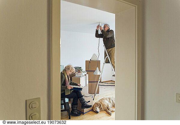 Senior couple in a new home with man mounting ceiling lamp