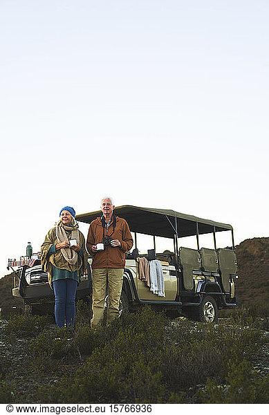 Senior couple on safari drinking tea outside off-road vehicle