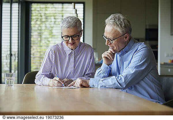 Senior couple sitting at table at home examining document