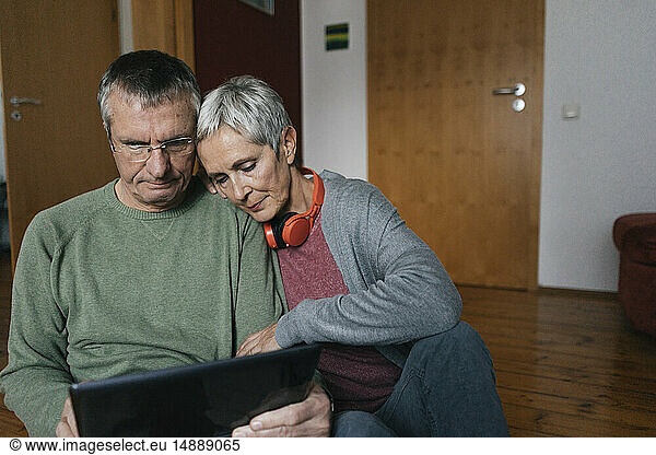 Senior couple sitting on the floor at home looking at tablet