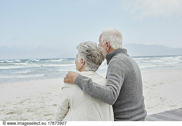 Senior couple standing on the beach with arms around