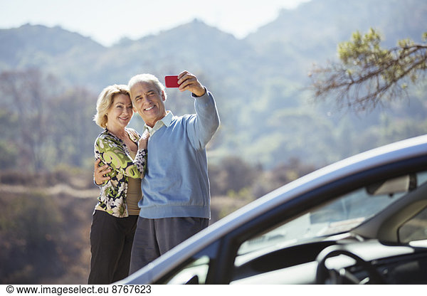 Senior couple taking self-portrait with cell phone outside car