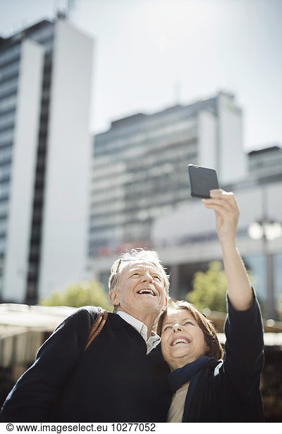 Senior couple taking selfie through smart phone in city