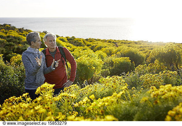 Senior couple talking while standing by flowering plants by sea