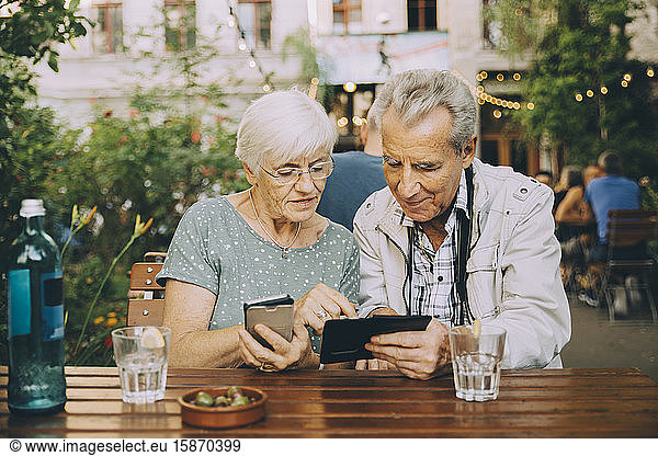 Senior couple using smart phone while sitting at restaurant in city