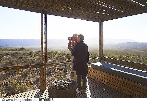 Senior couple with camera on sunny safari cabin balcony