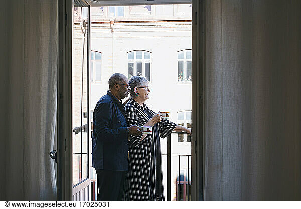Senior couple with coffee cup standing in balcony at home