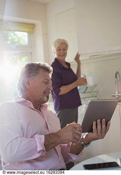 Senior couple with digital tablet talking in kitchen