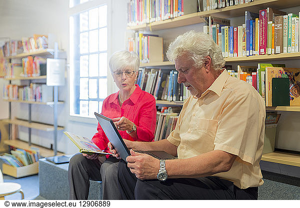 Senior couple with laptop and book in a city library