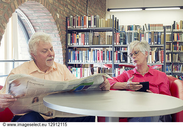 Senior couple with newspaper and e-book in a city library