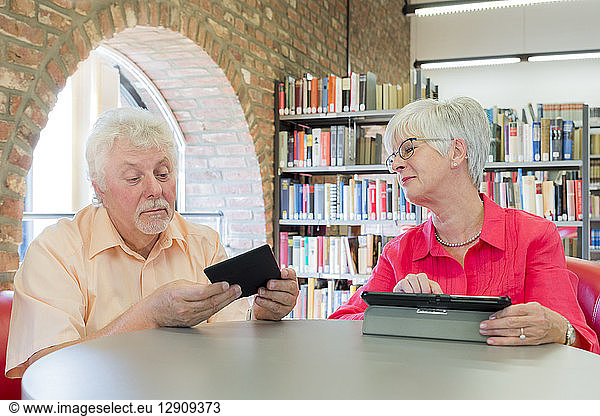Senior couple with tablet and e-book in a city library