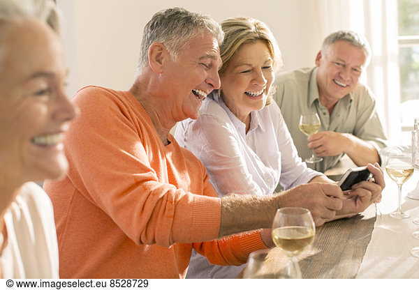 Senior couples drinking wine and looking at cell phone