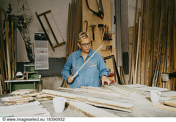 Senior craftswoman measuring timber on workbench at repair shop