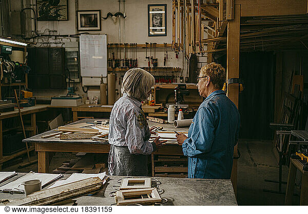 Senior craftswomen discussing together while working at repair shop