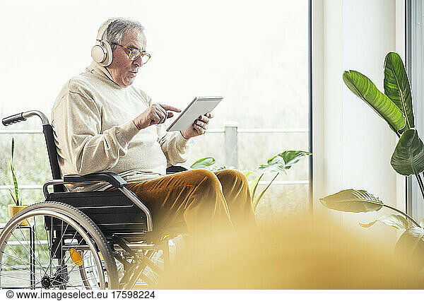 Senior disabled man using tablet PC on wheelchair at home
