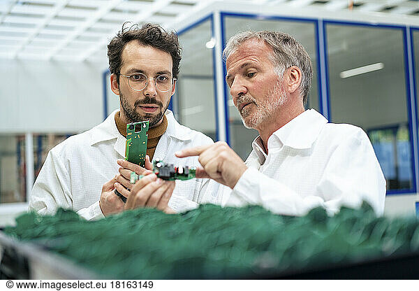 Senior engineer discussing over circuit board with colleague at industry