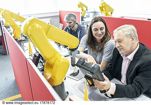 Senior engineer looking at digital control of female coworker at industrial robot