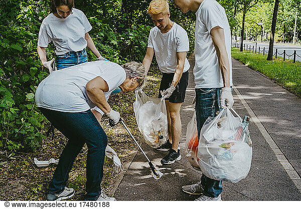 Senior female activist picking up face mask while cleaning park with young volunteers