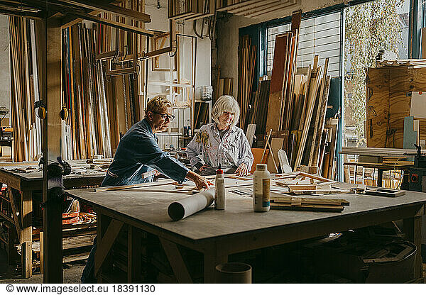 Senior female carpenter assisting colleague while working at repair shop